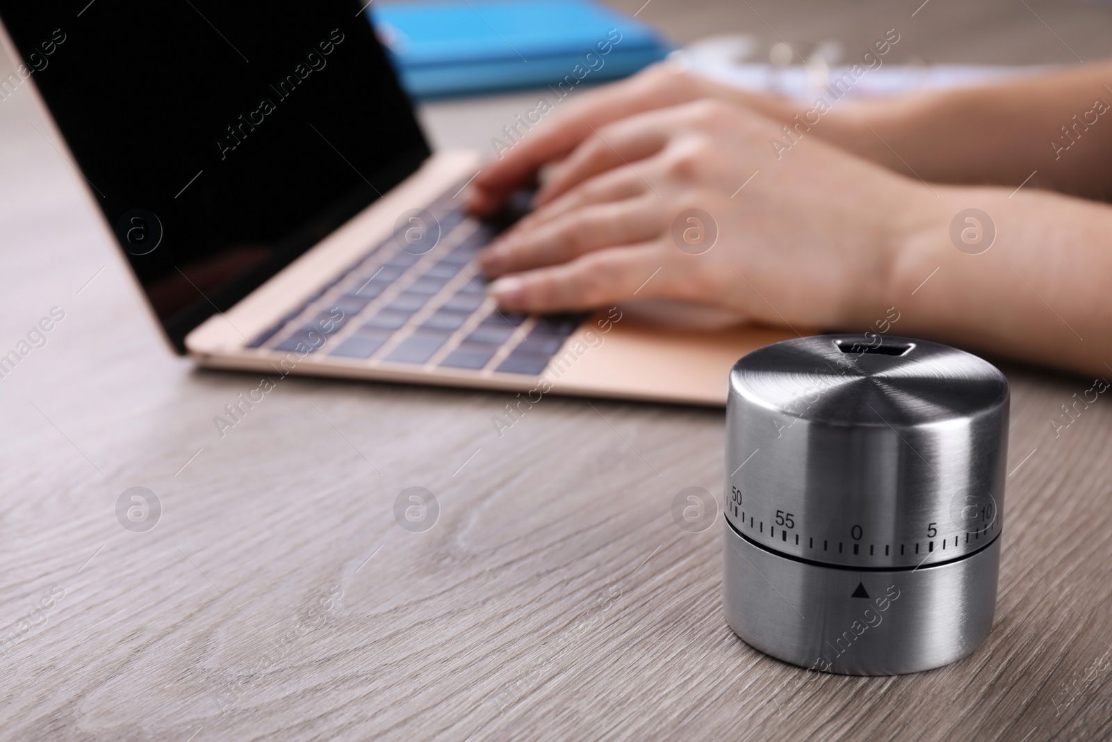 Photo of Woman working on laptop at wooden table, focus on kitchen timer. Space for text