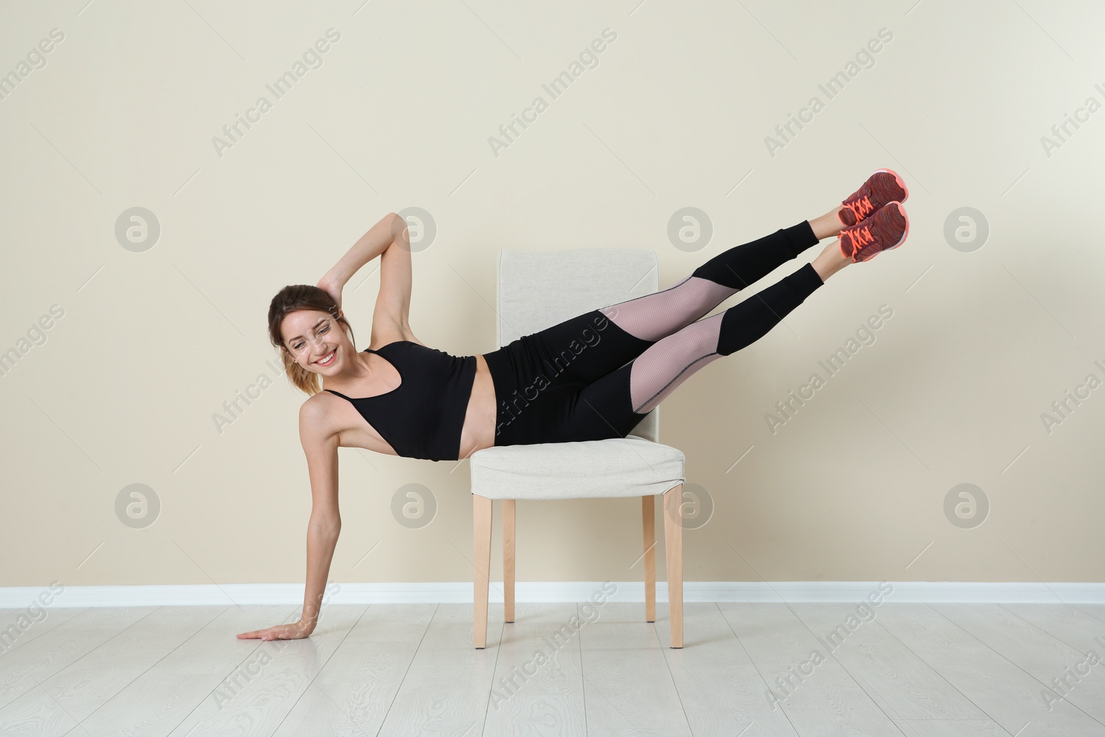 Photo of Young woman exercising with chair near color wall. Home fitness