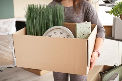 Photo of Young woman holding moving box with office stuff indoors, closeup