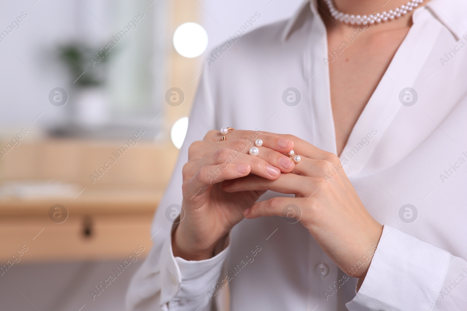Photo of Young woman trying on elegant rings with pearls indoors, closeup. Space for text