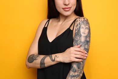 Photo of Beautiful woman with tattoos on arms against yellow background, closeup