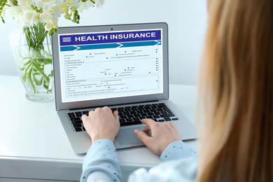 Woman with modern laptop indoors, closeup. Health insurance