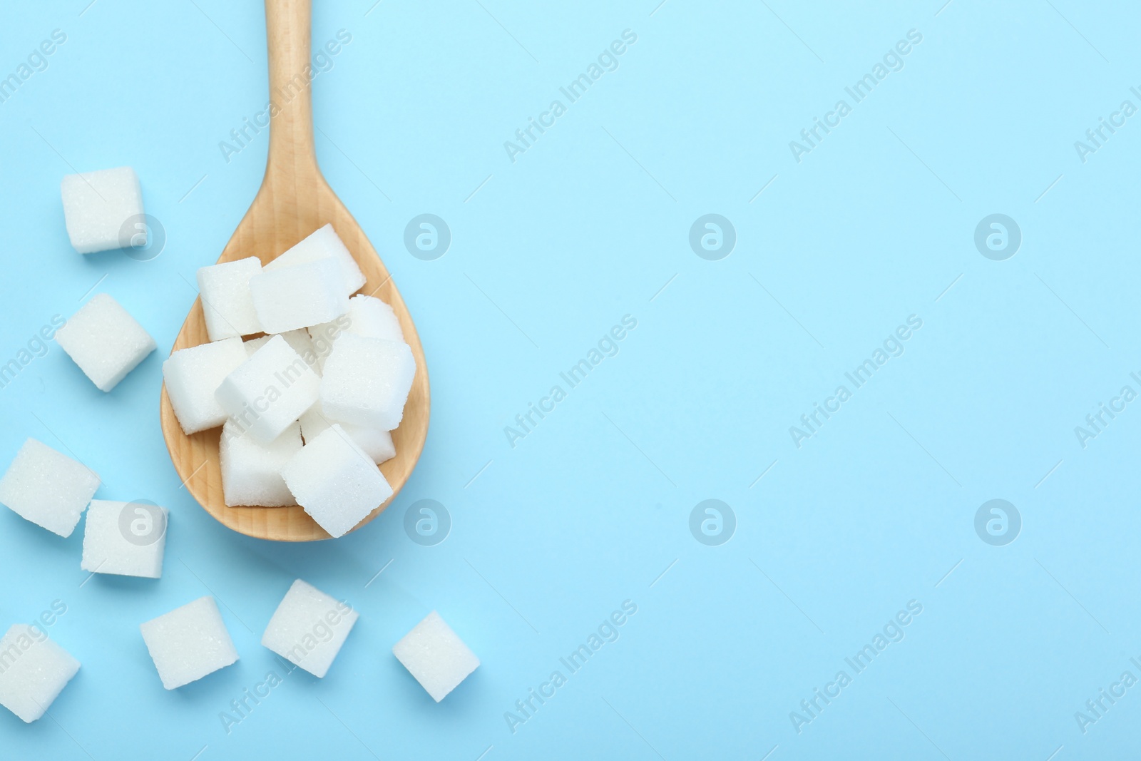 Photo of White sugar cubes and wooden spoon on light blue background, top view. Space for text