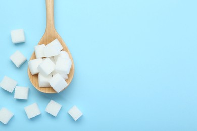 Photo of White sugar cubes and wooden spoon on light blue background, top view. Space for text