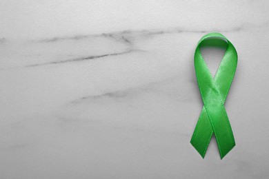World Mental Health Day. Green ribbon on white marble table, top view with space for text