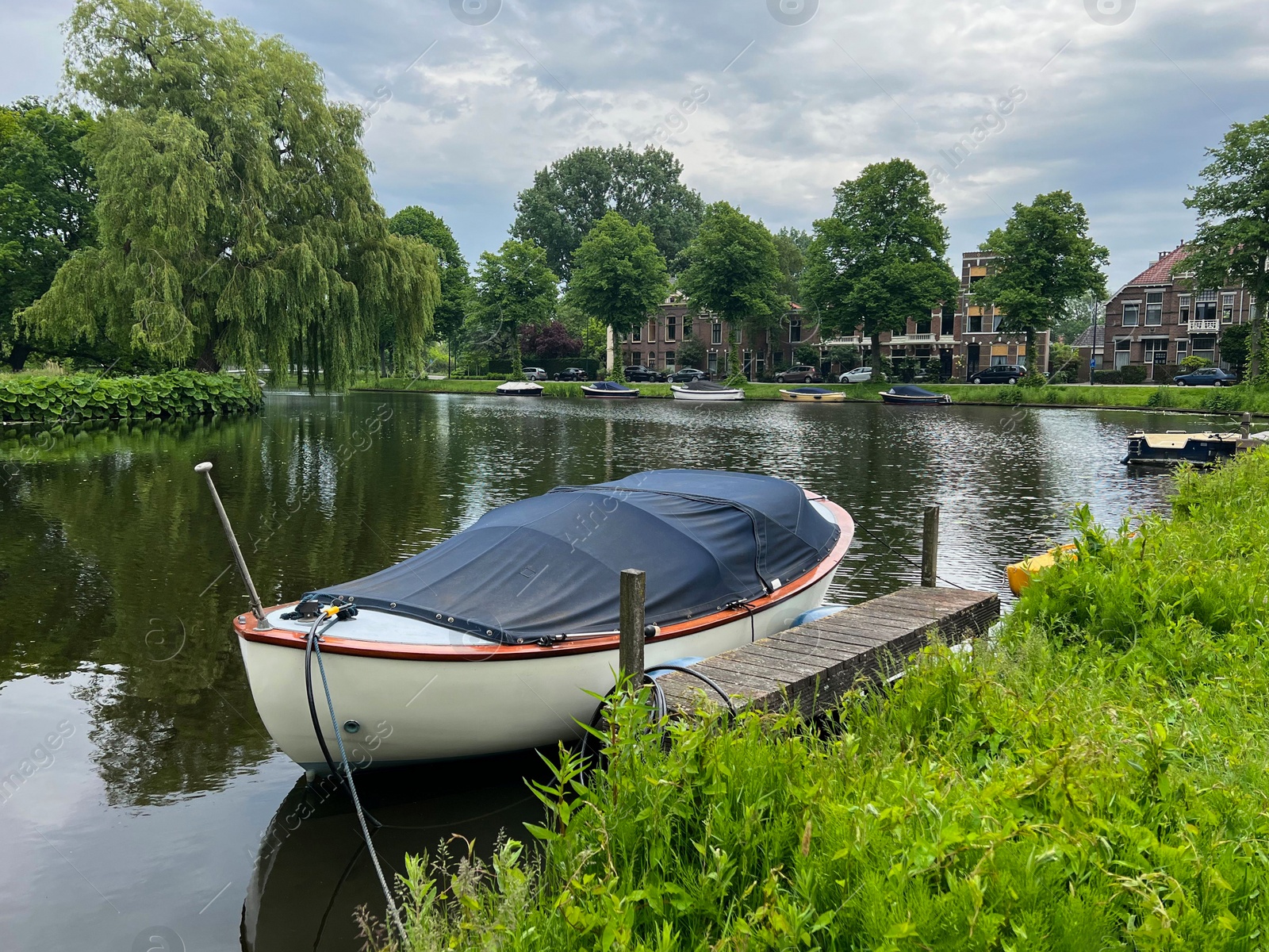 Photo of Beautiful view of city canal with moored boat surrounded by greenery