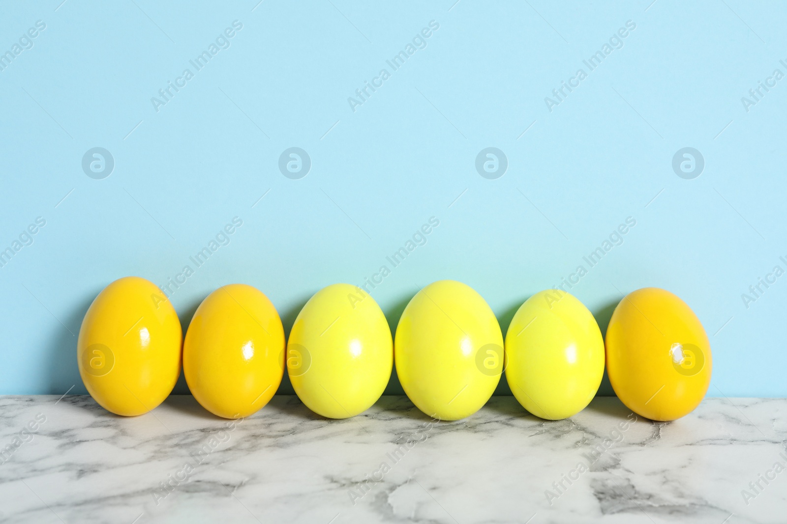 Photo of Easter eggs on white marble table against light blue background, space for text