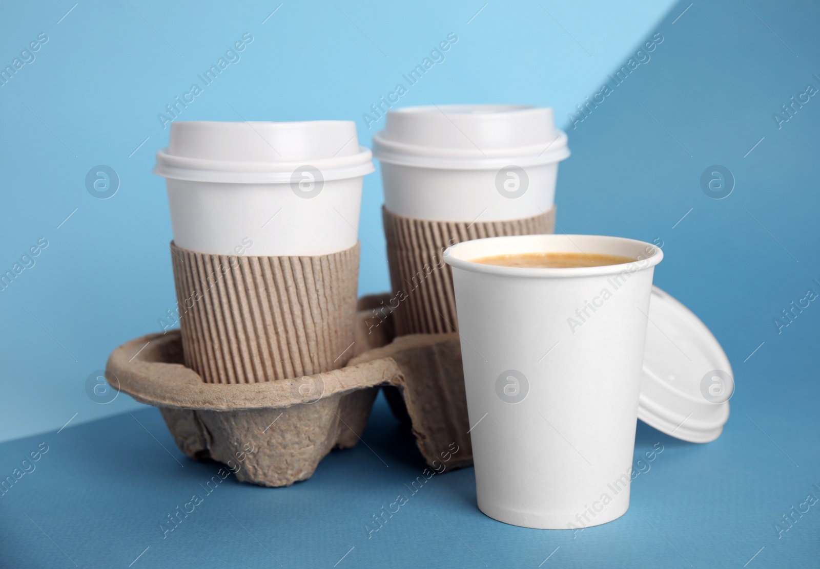 Photo of Takeaway paper coffee cups with sleeves, plastic lids and cardboard holder on blue background