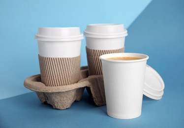Takeaway paper coffee cups with sleeves, plastic lids and cardboard holder on blue background