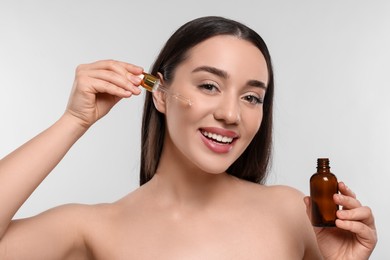 Happy young woman with bottle applying essential oil onto face on white background