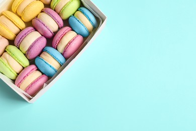 Many delicious colorful macarons in box on light blue background, top view. Space for text