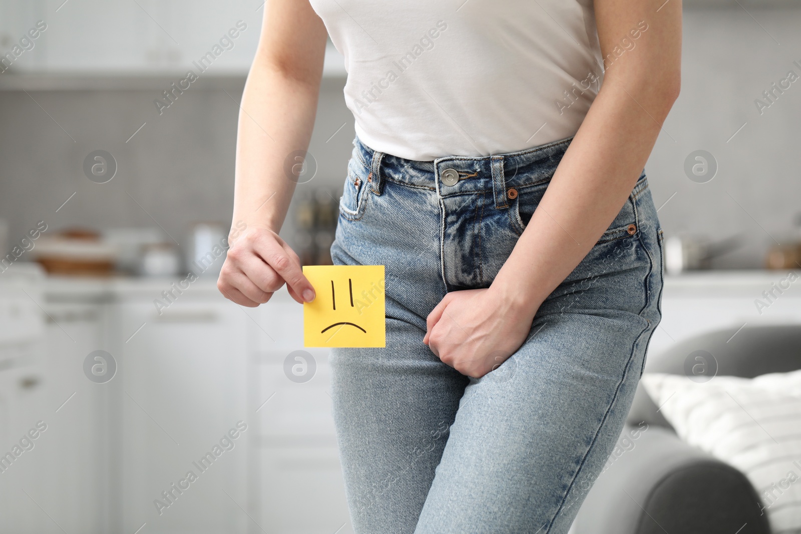 Photo of Woman holding sticky note with drawn sad face and suffering from cystitis at home, closeup