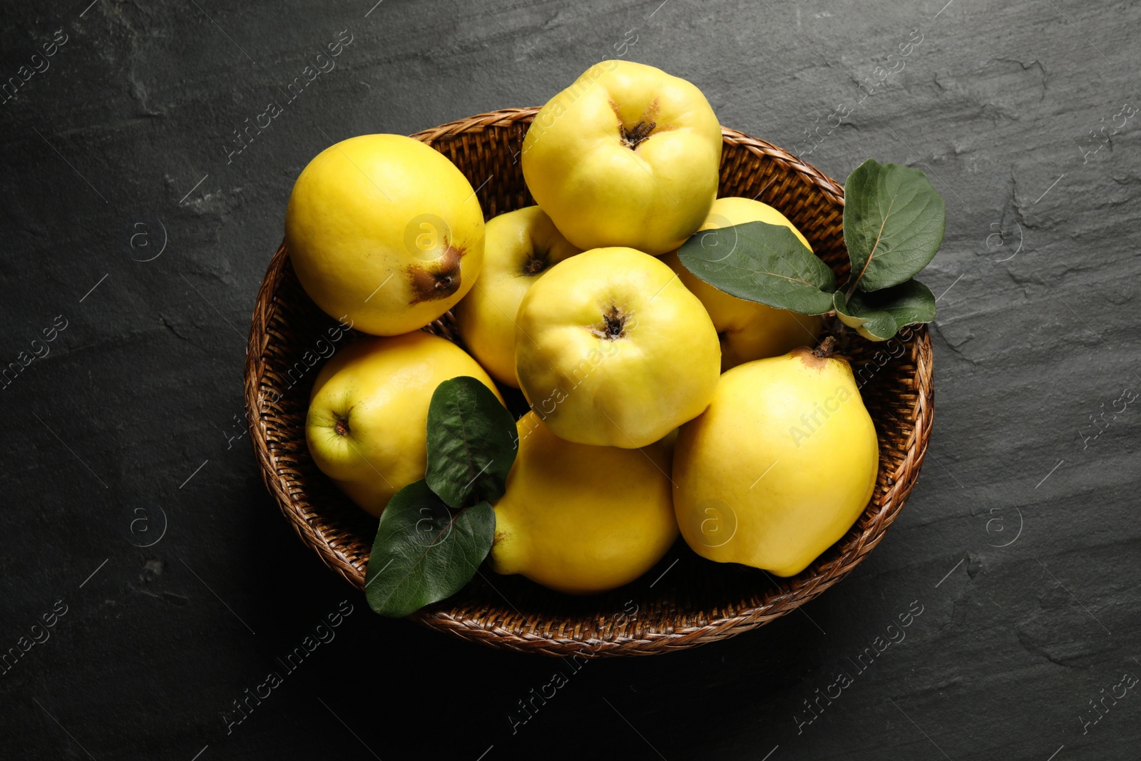 Photo of Fresh ripe organic quinces with leaves in wicker basket on black table, top view