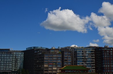 Modern airplane in sky over buildings on sunny day