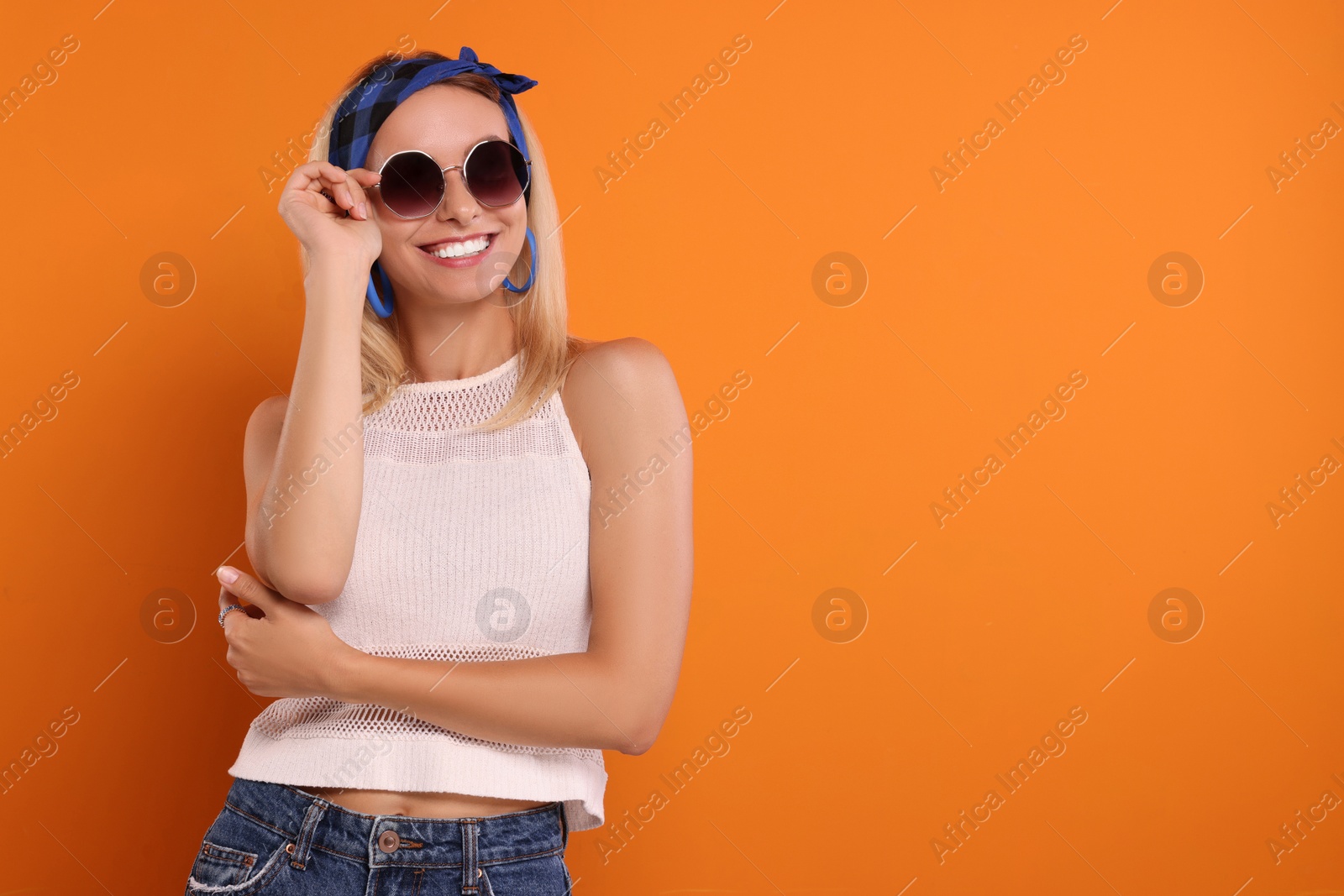 Photo of Portrait of smiling hippie woman in sunglasses on orange background. Space for text