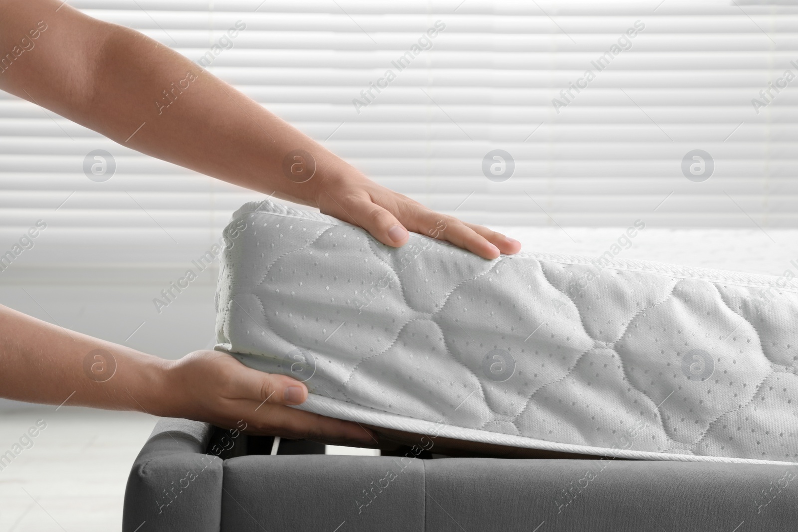 Photo of Woman putting soft light green mattress on gray bed indoors, closeup