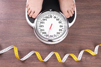 Photo of Closeup of woman using scales on floor near measuring tape, top view. Overweight problem