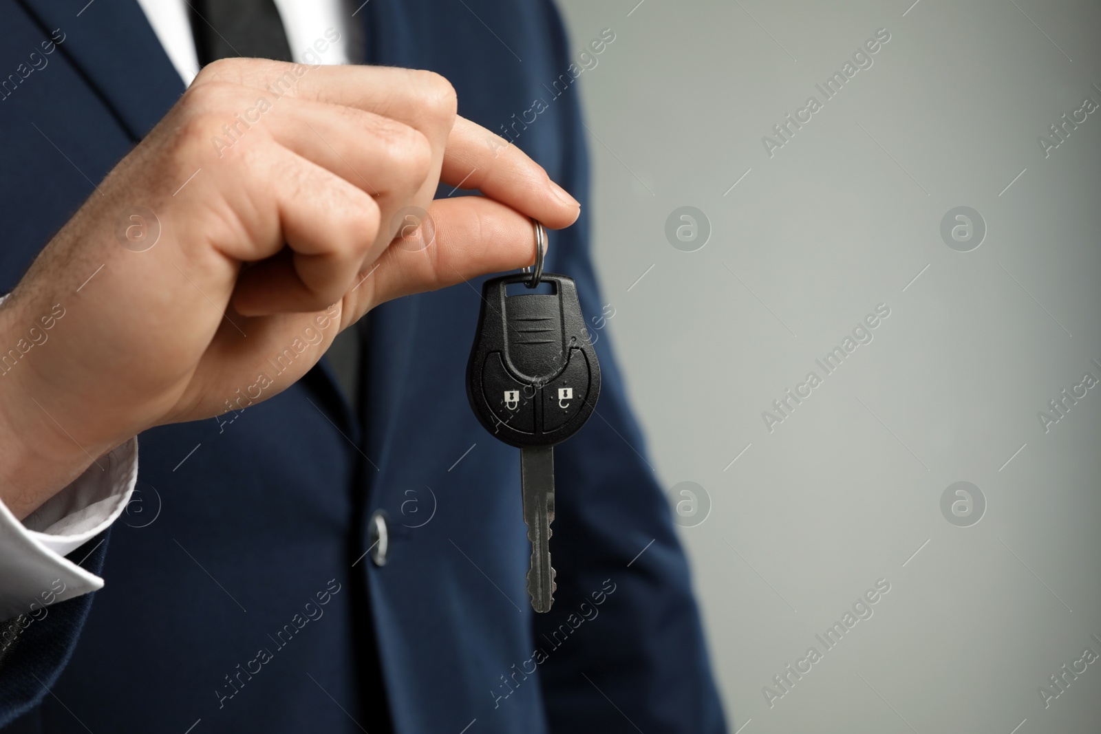 Photo of Young man holding car key on grey background, closeup. Space for text