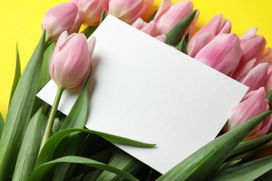 Beautiful pink spring tulips and blank card on yellow background, closeup. Space for text