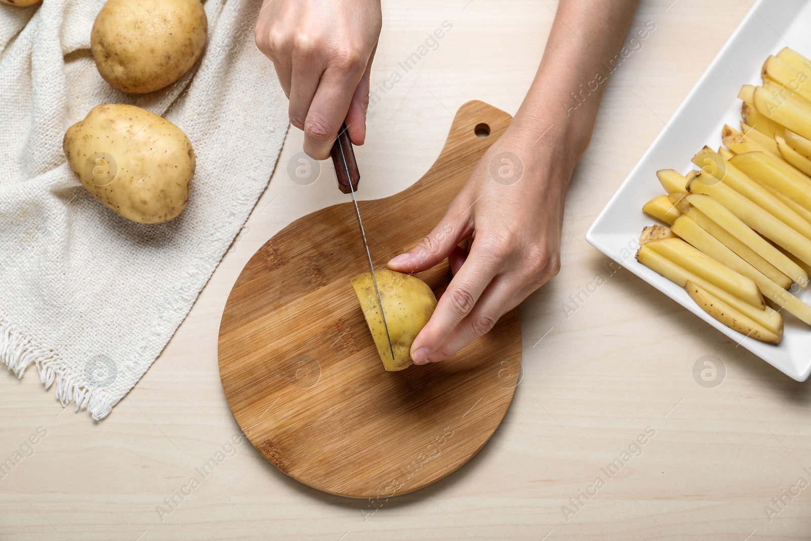 Photo of Woman cut potatoes at white wooden table, top view