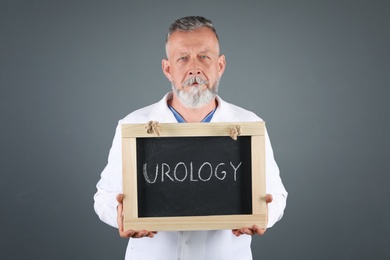 Photo of Male doctor holding chalkboard with word UROLOGY on grey background