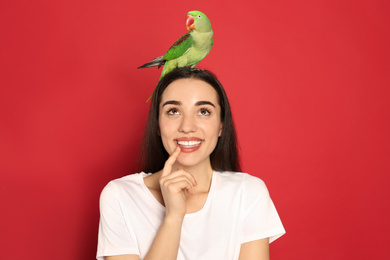 Photo of Young woman with Alexandrine parakeet on red background. Cute pet