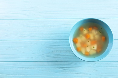 Bowl of fresh homemade soup to cure flu on wooden background, top view with space for text