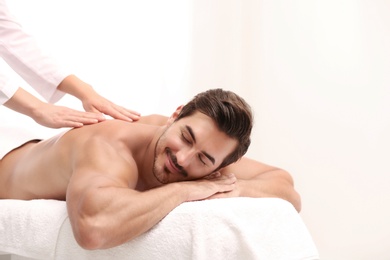 Photo of Handsome young man receiving back massage on light background, space for text. Spa salon