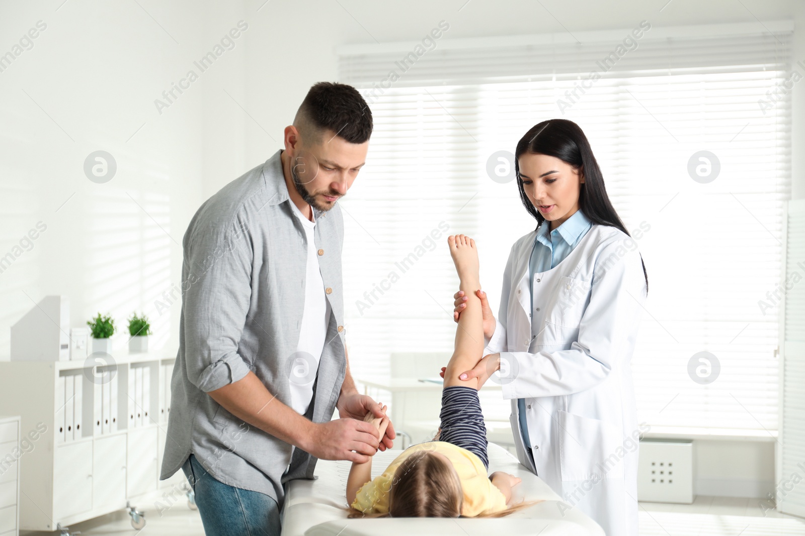 Photo of Professional orthopedist examining little patient's leg in clinic