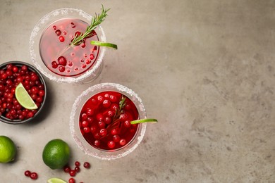 Photo of Tasty cranberry cocktail with rosemary and lime in glasses on grey table, flat lay. Space for text