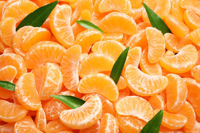 Photo of Fresh juicy tangerine segments with green leaves as background, top view