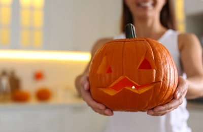 Photo of Woman holding pumpkin jack o'lantern indoors, closeup with space for text. Halloween celebration