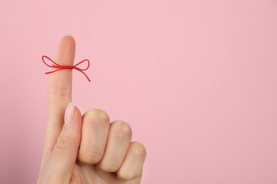 Photo of Woman showing index finger with tied red bow as reminder on pink background, closeup, Space for text