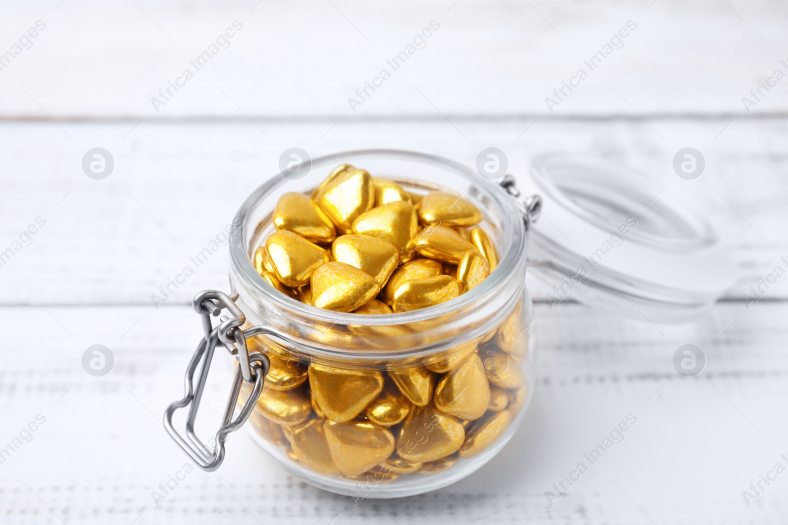 Photo of Jar with delicious heart shaped candies on white wooden table