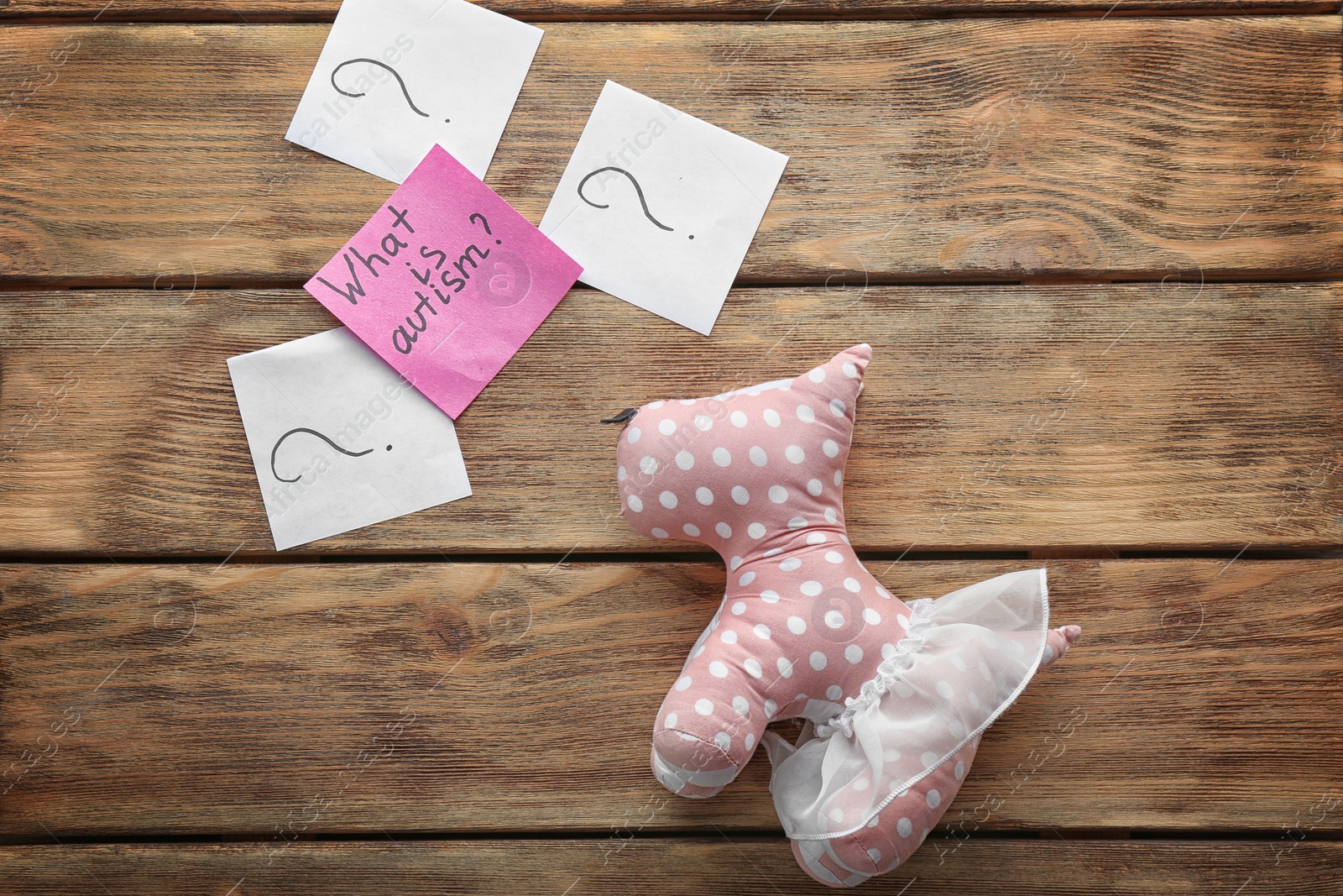 Photo of Toy and sticky note with phrase "What is autism?" on wooden background, flat lay