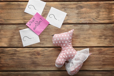 Toy and sticky note with phrase "What is autism?" on wooden background, flat lay