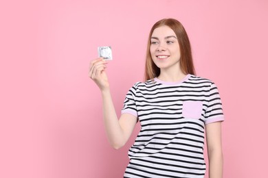 Photo of Woman holding condom on pink background. Safe sex