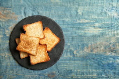 Slate plate with toasted bread on wooden background, top view