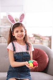 Photo of Little girl in bunny ears headband holding Easter eggs indoors