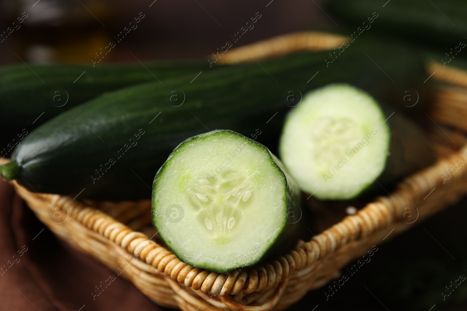 Photo of Fresh whole and cut cucumbers in wicker basket, closeup