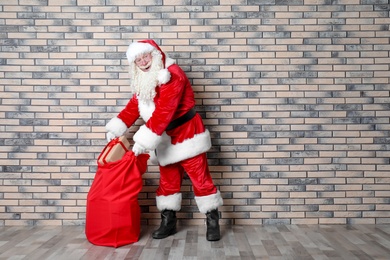 Photo of Authentic Santa Claus with big red bag full of gifts near brick wall