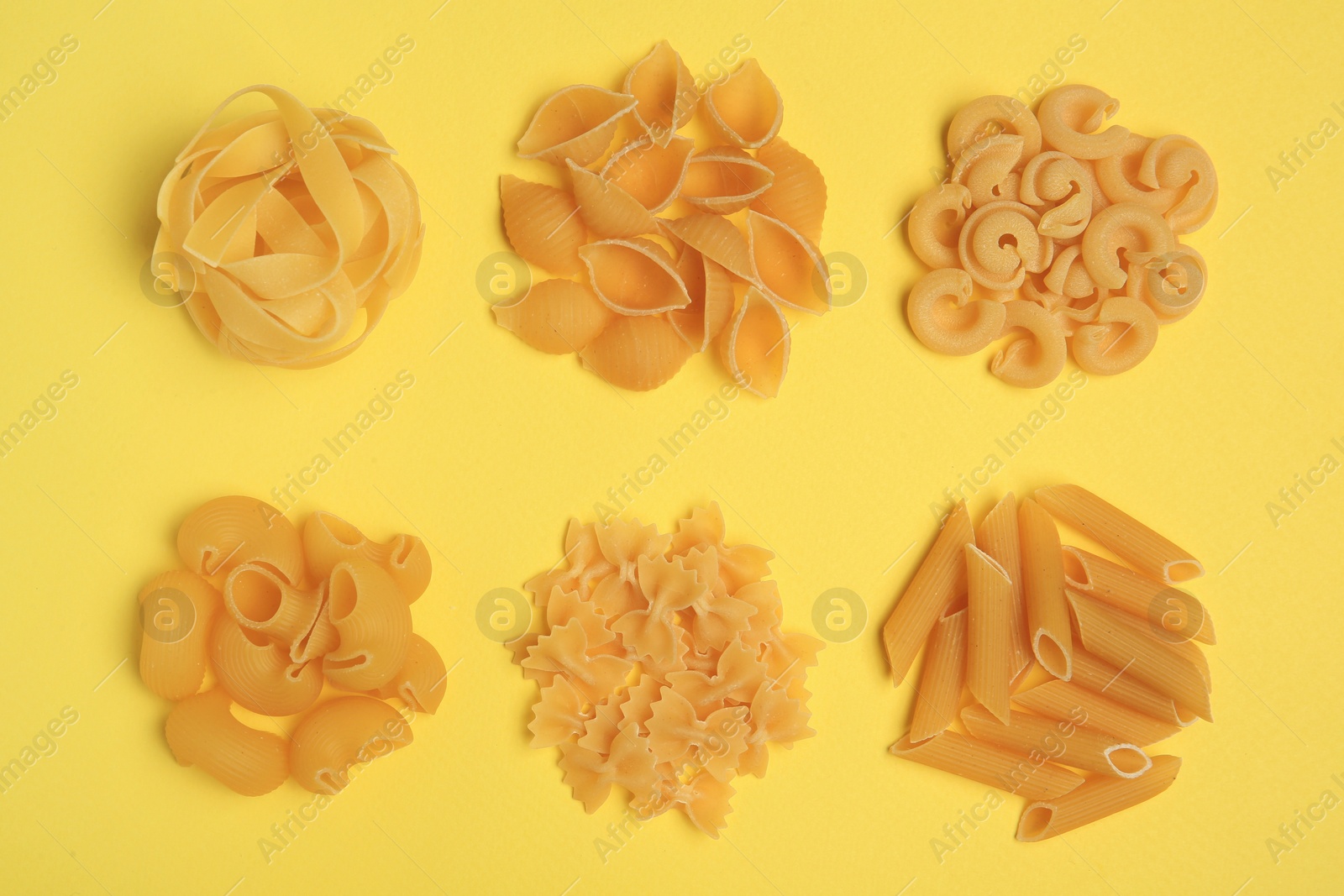 Photo of Different types of pasta on yellow background, flat lay