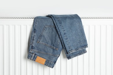 Blue jeans hanging on white radiator indoors