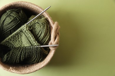 Photo of Knitting, needles and soft yarns on light green background, top view. Space for text