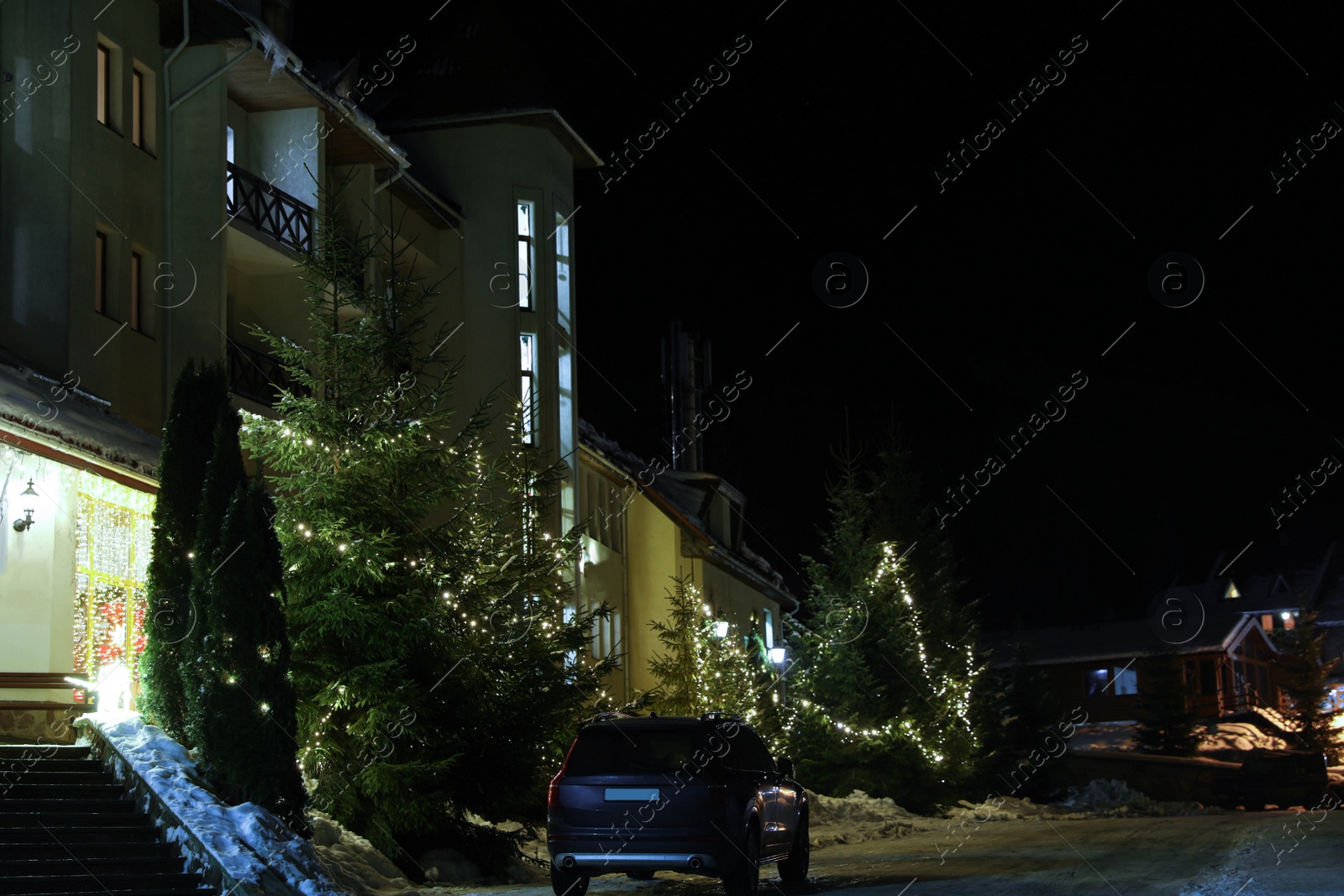 Photo of Modern car on snowy road near hotel at night. Winter vacation