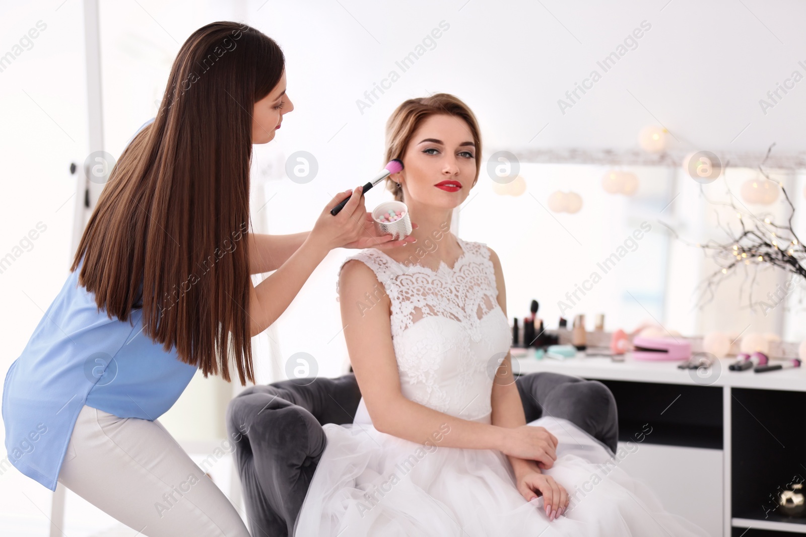 Photo of Makeup artist preparing bride before her wedding in room