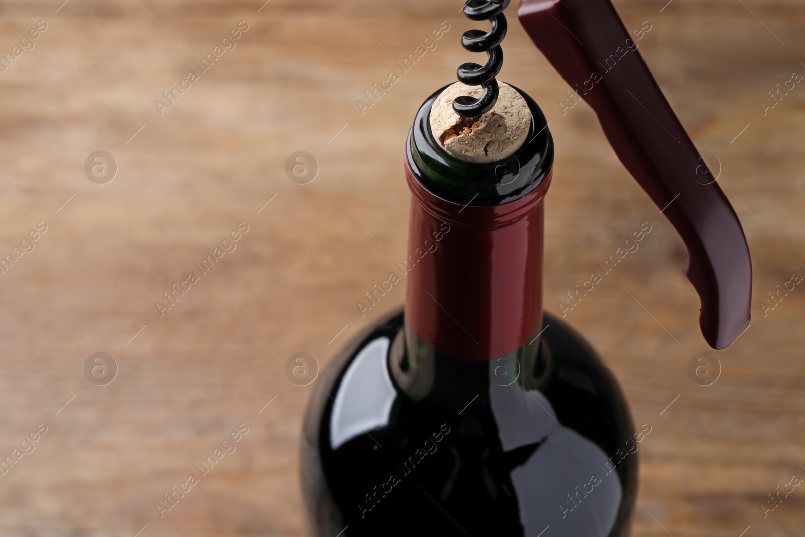 Photo of Opening wine bottle with corkscrew on table, closeup. Space for text