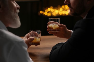Photo of Men with glasses of whiskey talking at wooden table in bar
