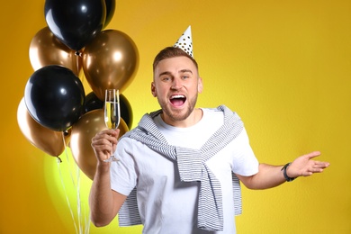 Portrait of happy man with champagne in glass and party balloons on color background