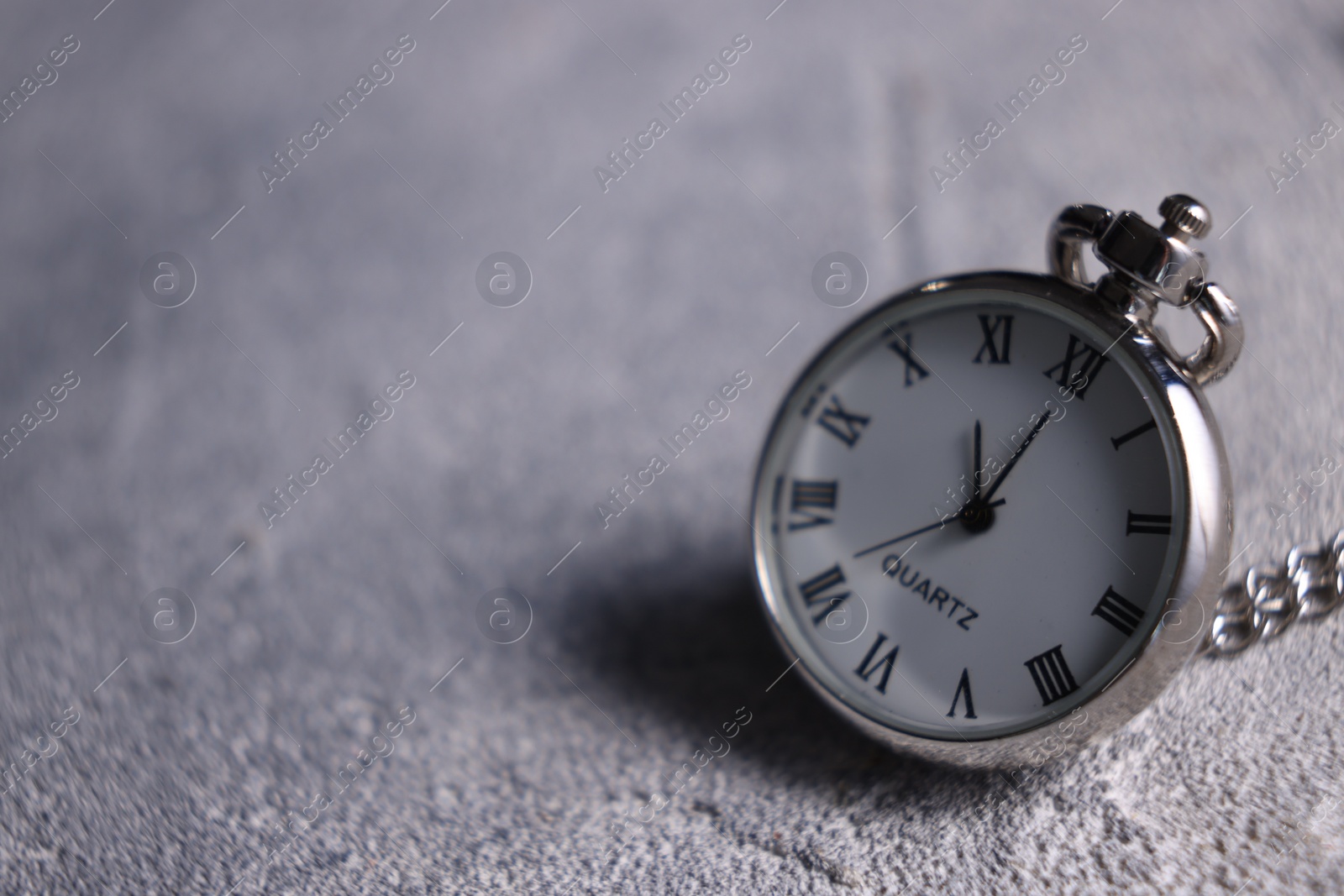 Photo of Silver pocket clock on grey textured table, closeup. Space for text